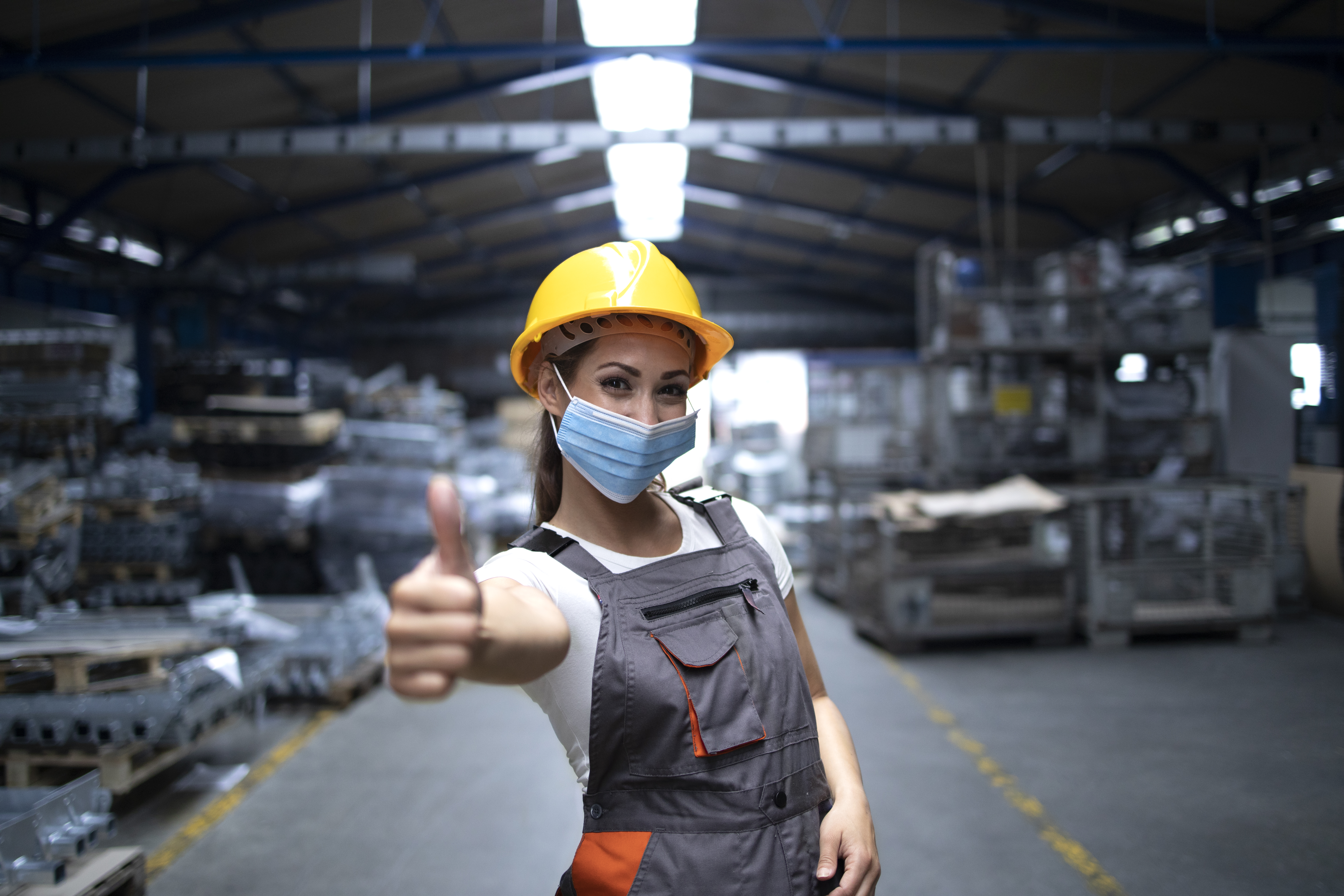 woman-standing-in-factory-hall-and-showing-thumbs-up-while-wearing-hygienic-mask-as-prevention-against-corona-virus.jpg
